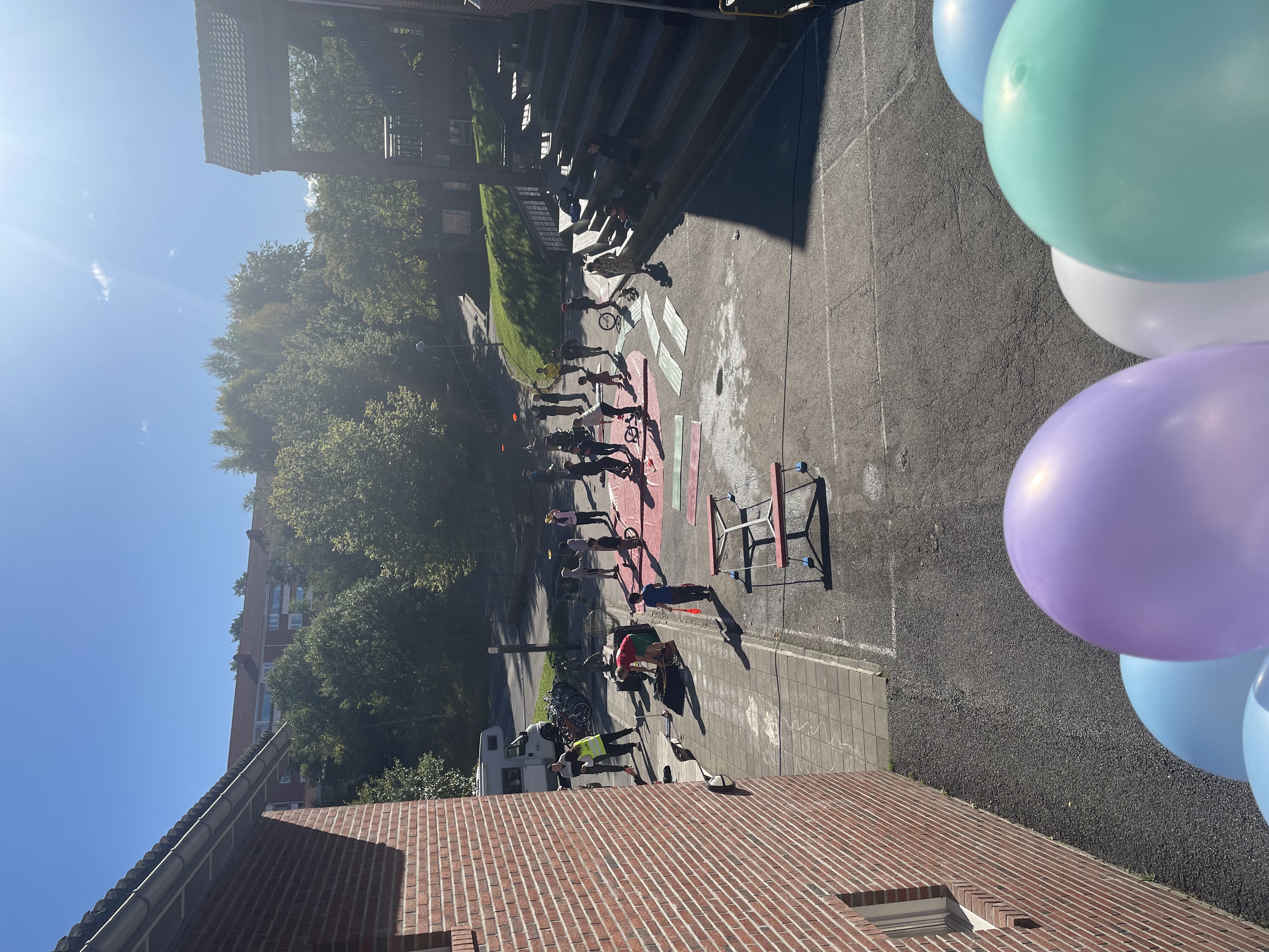 en gruppe mennesker som går rundt på en gårdsplass med trær og bygninger