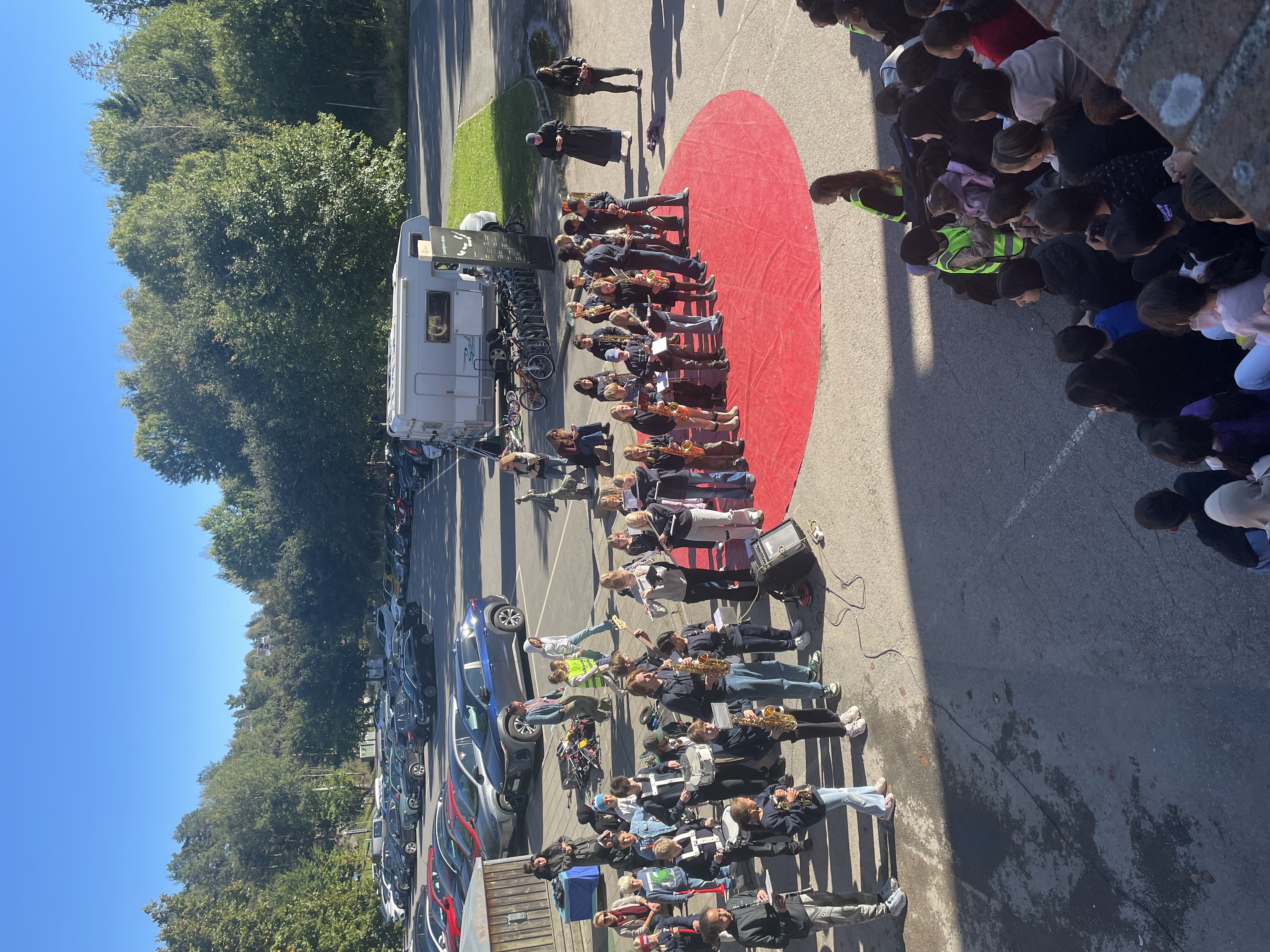 en gruppe mennesker som står på en vei med biler og trær i bakgrunnen